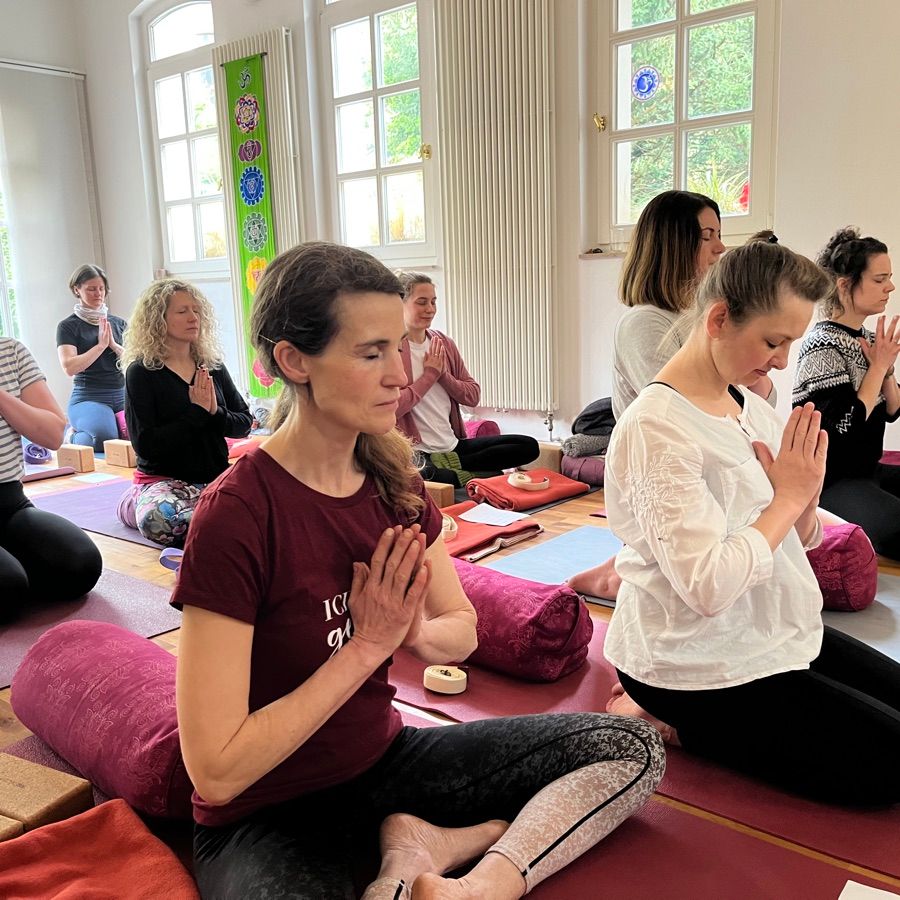Die Ausbildungsgruppe meditiert gemeinsam im Namaste-Sitz im Yogaraum