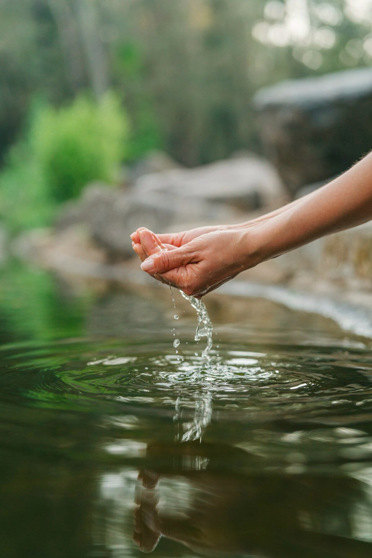 Zwei Hände schöpfen klares Wasser aus einem natürlichen Wasserbecken