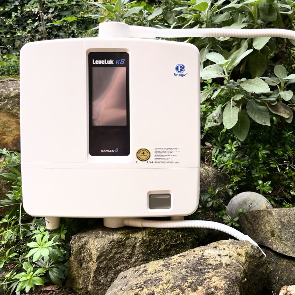 Das Kangen-K8-Gerät von Enagic zwischen Pflanzen und Natursteinen im Garten